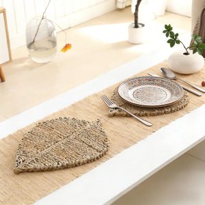 Leaf-shaped water hyacinth placemat with a decorative plate, fork, knife, and spoon on a linen runner